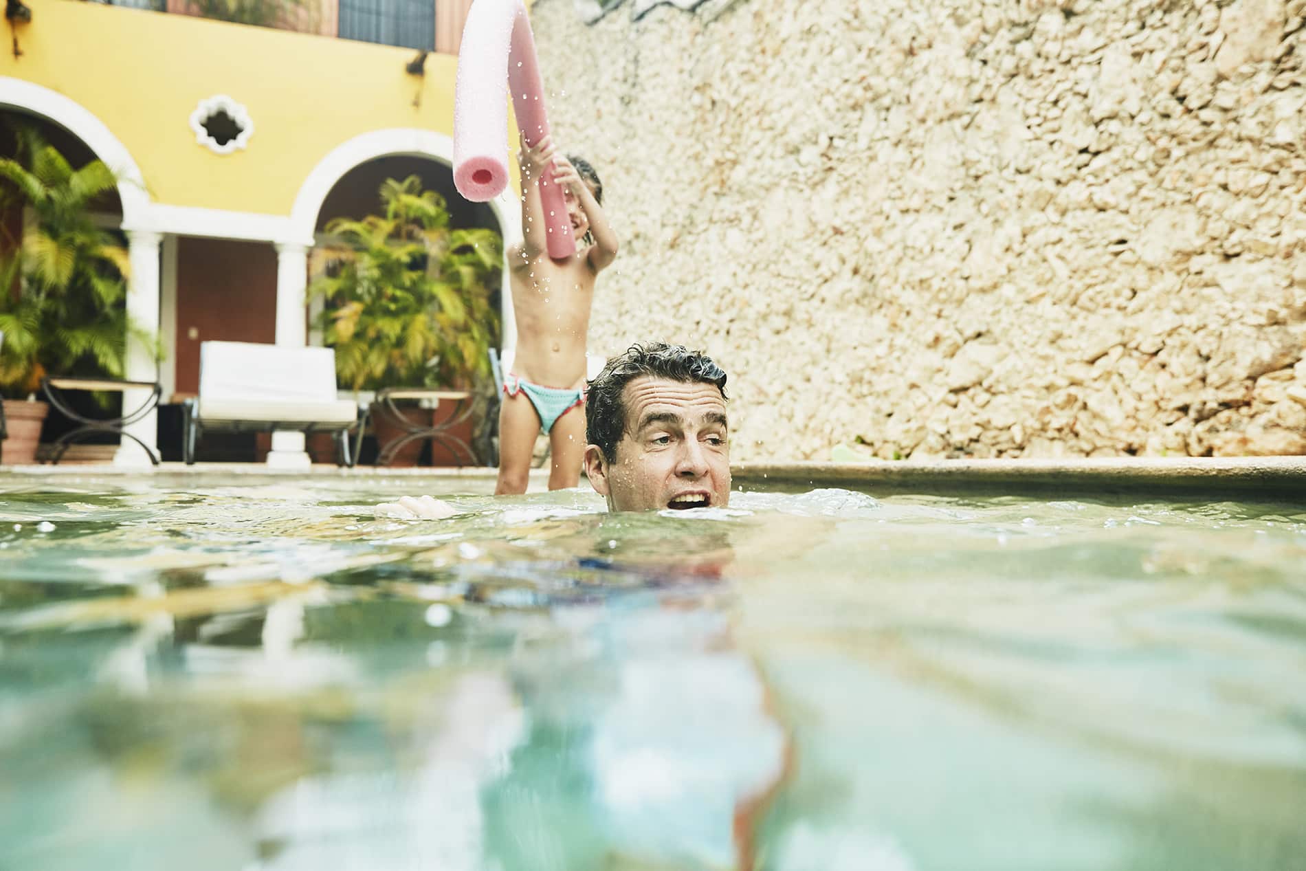 Father playing with daughter in pool at tropical resort